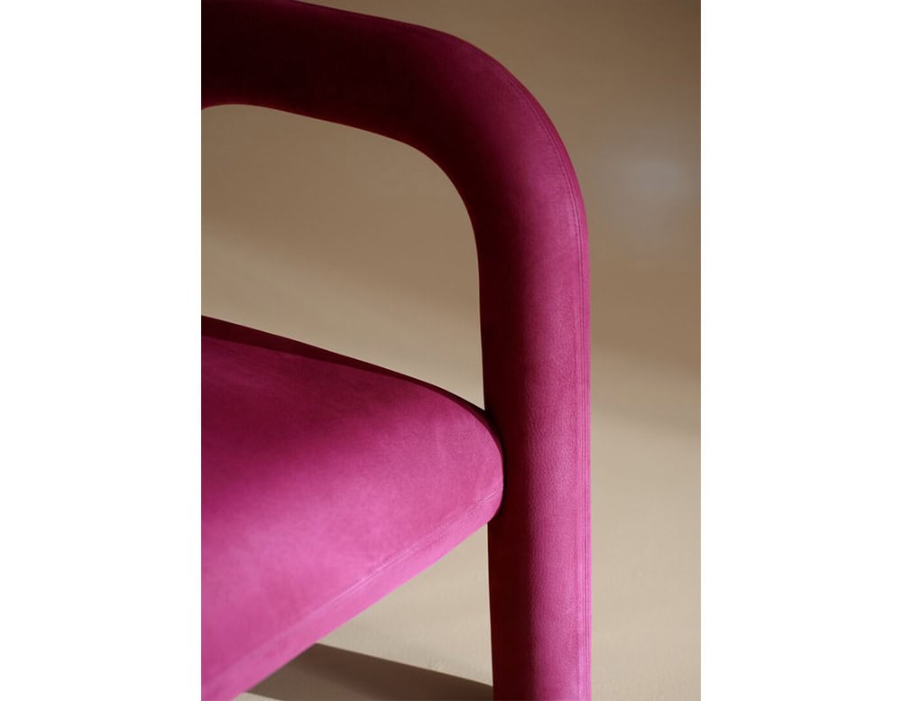 Close-up view highlighting its velvety magenta upholstery and sculpted armrest, showcasing the smooth curves and refined craftsmanship of its design.