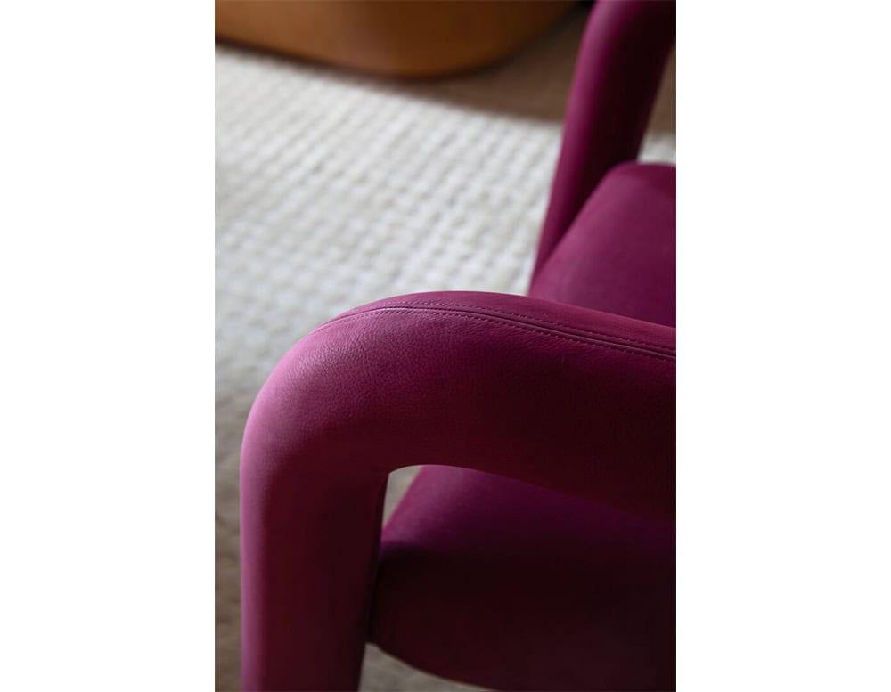 Detail of the Aimee Armchair’s plush magenta fabric and rounded structure, emphasizing its tactile luxury and the seamless flow of its contemporary silhouette.