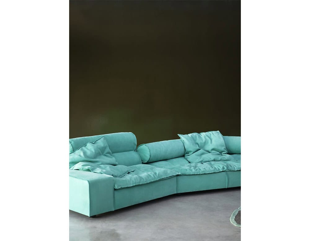 A plush, low-profile sofa upholstered in turquoise fabric, featuring oversized pillows and cylindrical supports that combine casual comfort with refined modern craftsmanship.