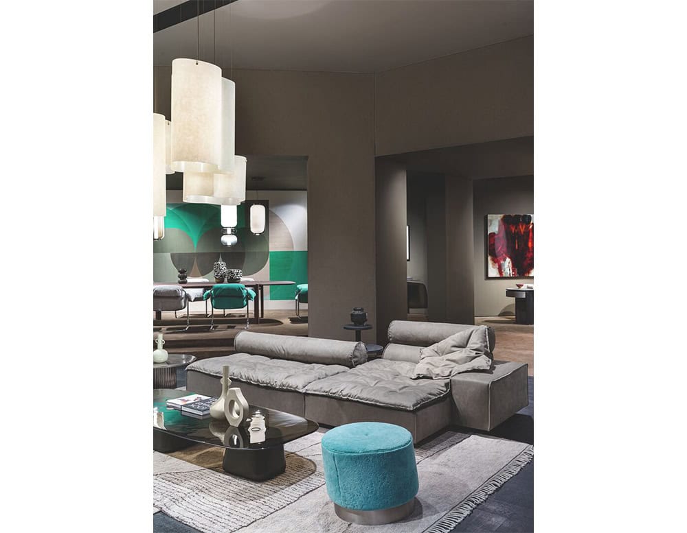 A modular gray sofa with plush seating and cylindrical backrests defines a contemporary lounge setting paired with a turquoise pouf, sculptural coffee table, and layered neutral rug for balance and texture.