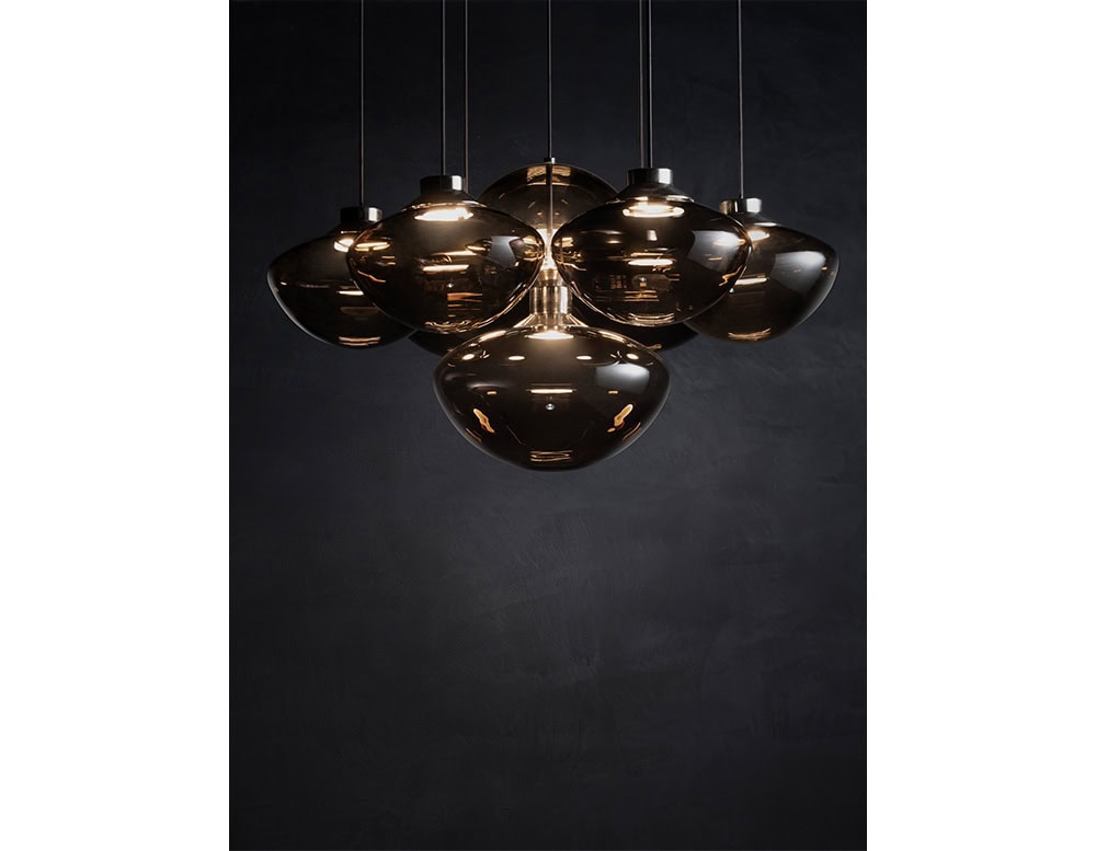 A cluster of seven hand-blown glass pendants in smoky tones creates a dramatic centerpiece. The organic, fluid shapes diffuse a warm glow, offering both sculptural beauty and ambient illumination.