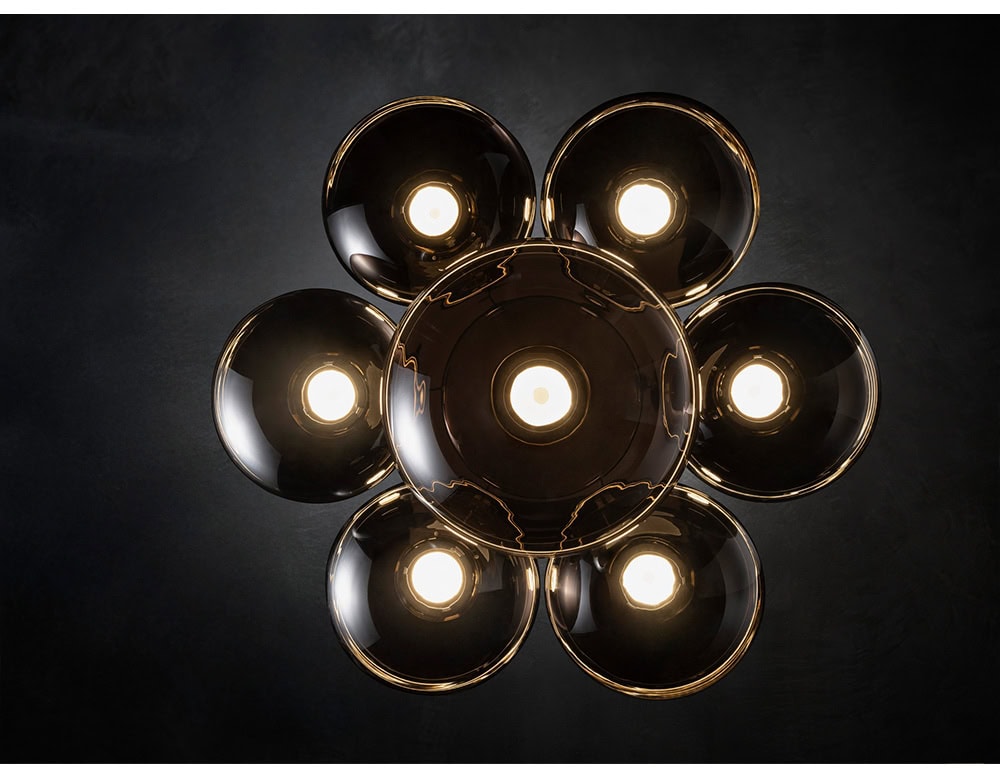 A close-up of the Floyd Seven ceiling light reveals the refined interplay of metal and glass. The polished fittings reflect the warm glow from within, emphasizing craftsmanship and subtle elegance.