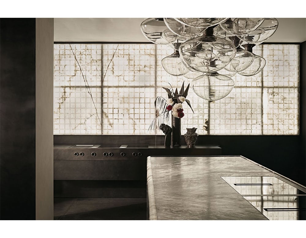 A composition of smoked glass pendants from the Floyd Seven collection enhances a minimalist kitchen. The sculptural light fixture reflects the textured surfaces and complements the elegant, modern setting.