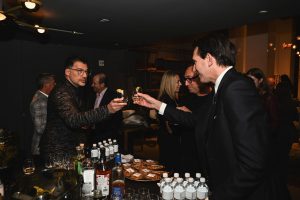 Guests share a cheerful toast at the bar, raising their glasses with genuine smiles as the party buzzes around them.