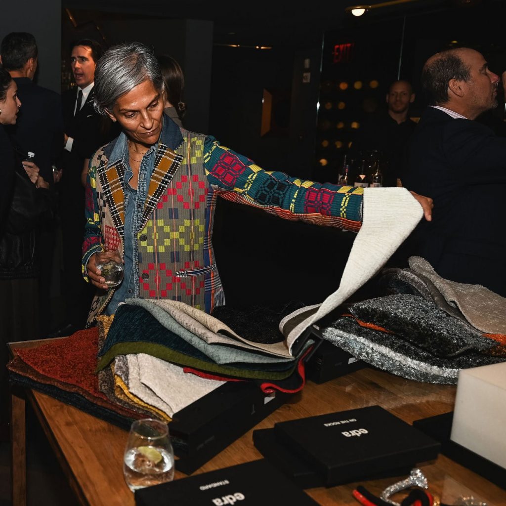 A guest explores a selection of luxurious fabric samples, appreciating textures and tones while enjoying a drink during the lively showroom event.
