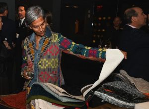 A guest thoughtfully examines a selection of textured fabric samples while holding a drink, showcasing a moment of curiosity and tactile appreciation during the event.