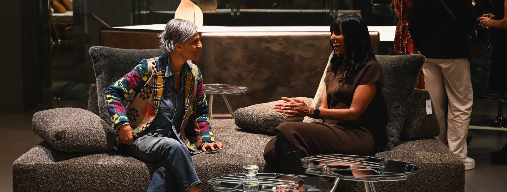 Two people sit on a textured sofa in a warm modern setting, engaged in a lively conversation with soft lighting and contemporary decor enhancing the inviting atmosphere.
