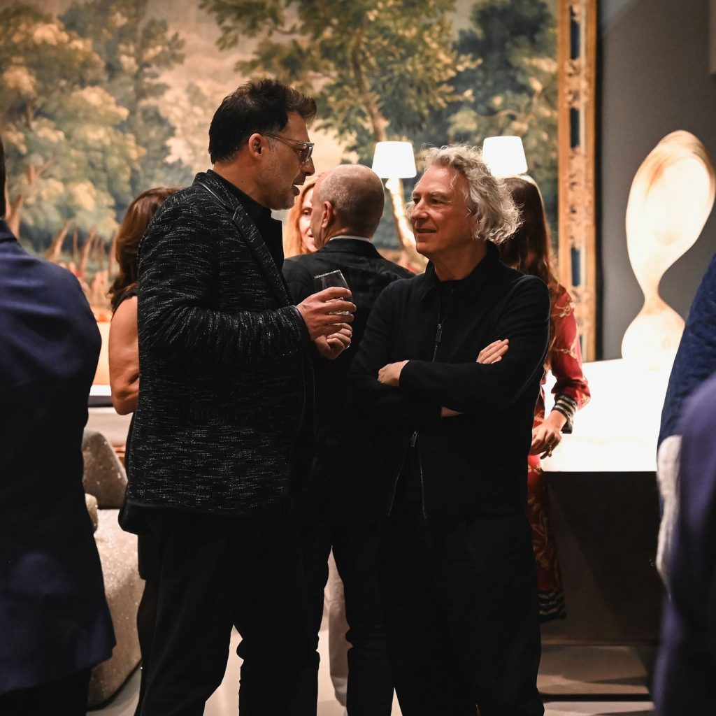 A relaxed chat unfolds as guests enjoy the elegant atmosphere of the showroom, surrounded by beautiful art and inviting design pieces that set a welcoming tone for the evening.