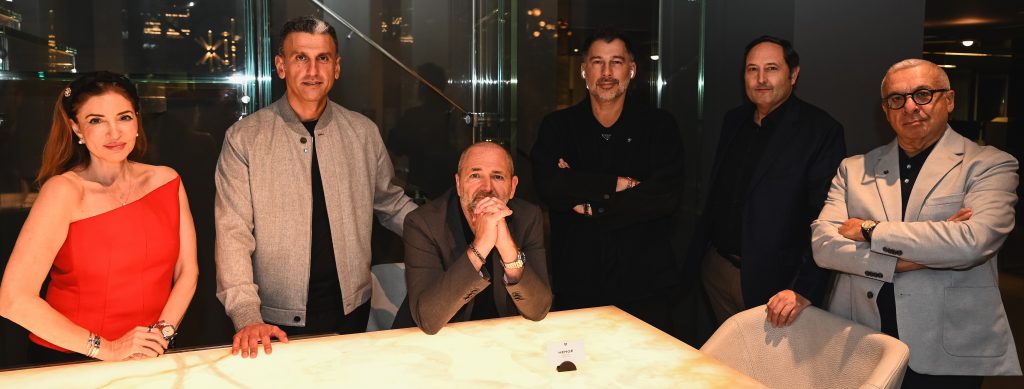 A group of six people gathered around a lighted table in a modern interior, all dressed elegantly and smiling, creating a warm and friendly event atmosphere.