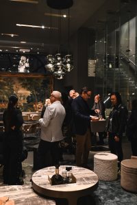 Guests mingle in a stylish interior, chatting around modern tables and under reflective pendant lights, creating a warm and lively event atmosphere.