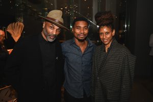 Three people pose together in a warm modern interior, smiling and standing close as soft lighting and contemporary decor create an inviting event atmosphere.
