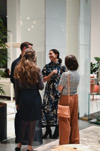 A small group of people stand together in a modern interior, enjoying a friendly conversation amid soft lighting, stylish decor, and a relaxed event atmosphere.