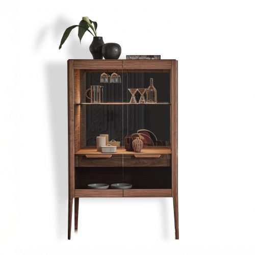 Tall wooden bar cabinet with refined proportions featuring a warm wood frame glass doors and interior shelving designed to display glassware and objects combining functional storage with an elegant vertical silhouette and crafted detailing.