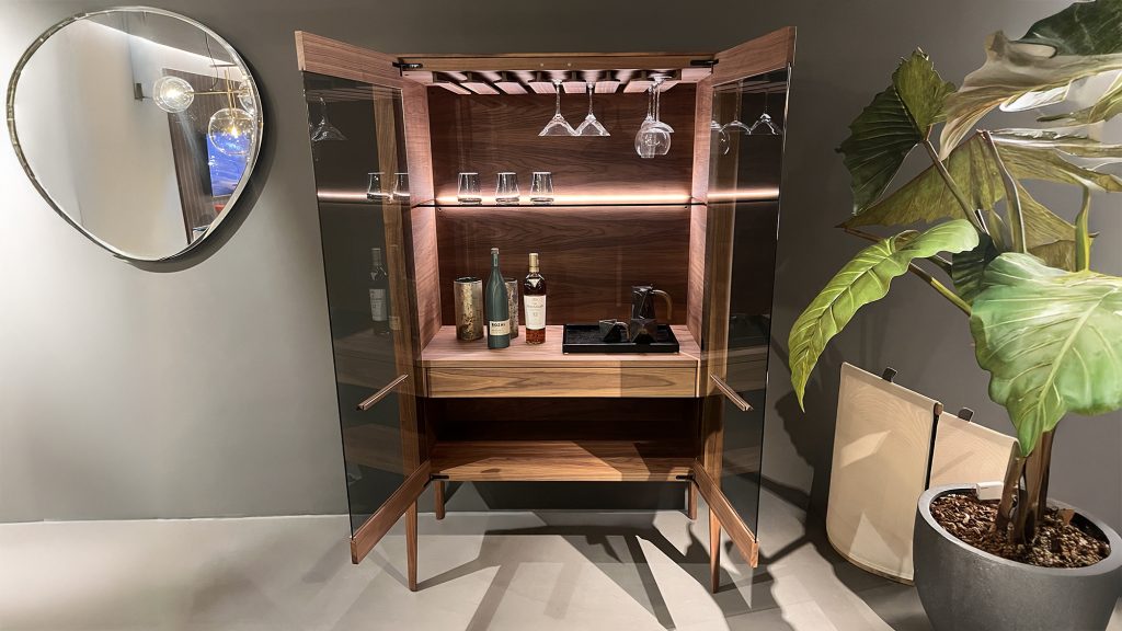 Atlante bar cabinet by Porada crafted in solid walnut with glass doors integrated stemware holders and soft interior lighting offering a refined storage solution that highlights bottles glassware and accessories with clean architectural lines.