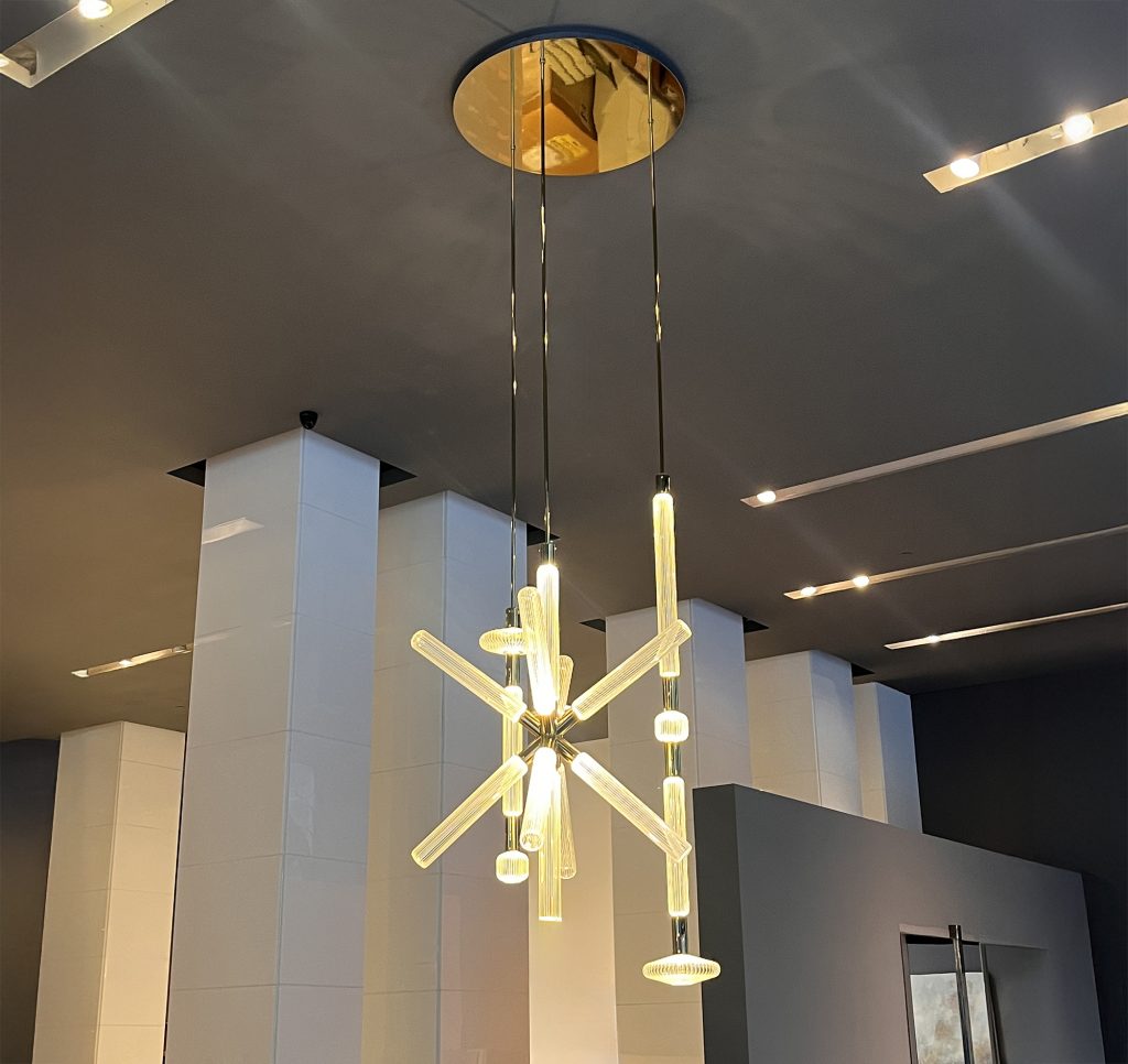 Cipher suspension by Lasvit featuring slender handblown glass tubes suspended from a brass canopy forming a radiant starburst that highlights fine craftsmanship warm light and sculptural elegance.