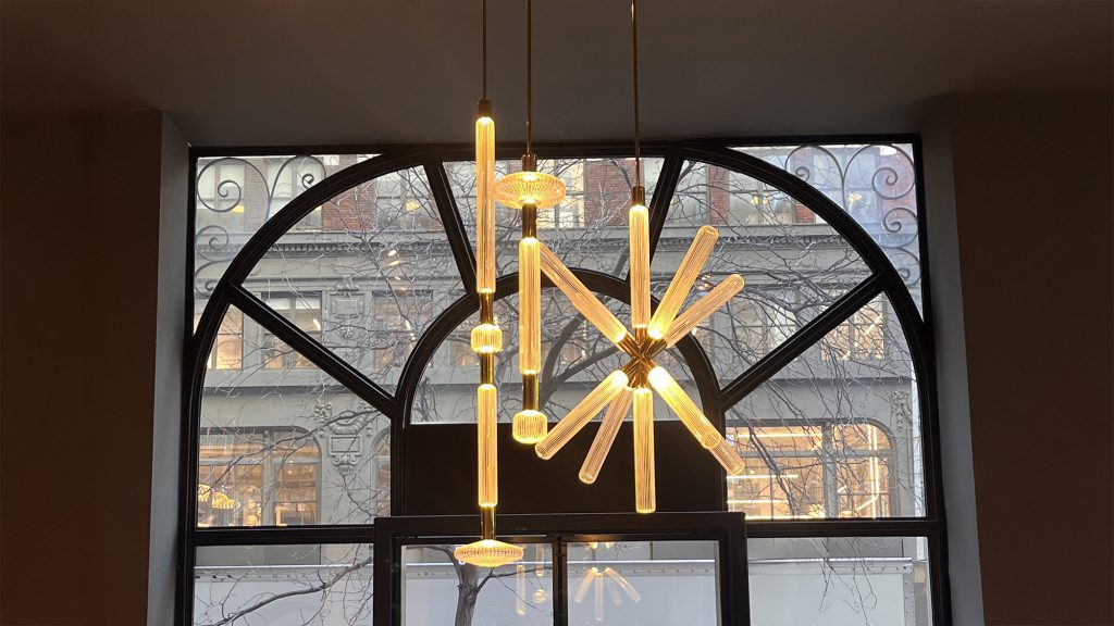 Lasvit Cipher suspension light featuring illuminated glass rods arranged in a sculptural radial composition with warm amber glow highlighting the craftsmanship and transparency of the glass while creating a striking focal point within the space.