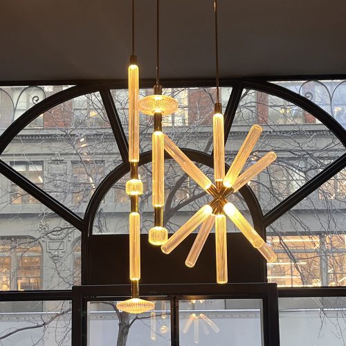 Lasvit Cipher suspension light featuring illuminated glass rods arranged in a sculptural radial composition with warm amber glow highlighting the craftsmanship and transparency of the glass while creating a striking focal point within the space.