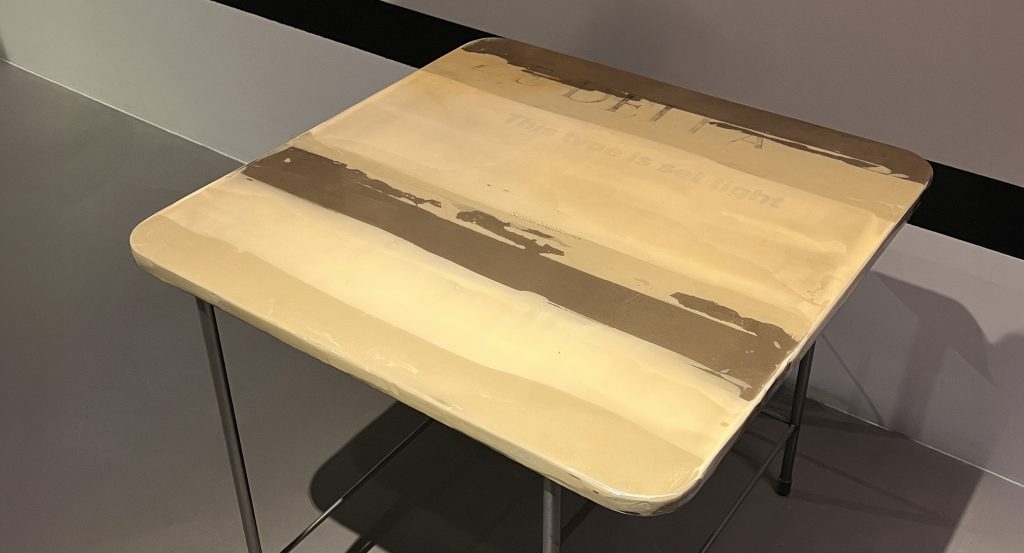 This small table features a soft yellow top with layered beige and warm taupe tones that give it a handcrafted look. The slim metal base adds contrast and keeps the design light, making it ideal as a side or accent table.