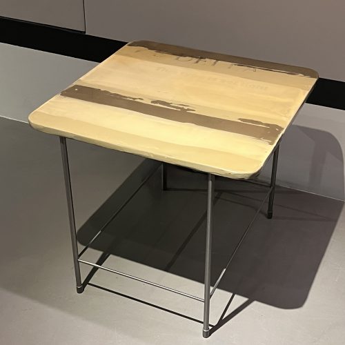 A compact side table featuring a warm yellow surface with a soft layered finish. The slim metal frame adds contrast and stability, making it a versatile accent piece for living areas, bedrooms, or reading corners.