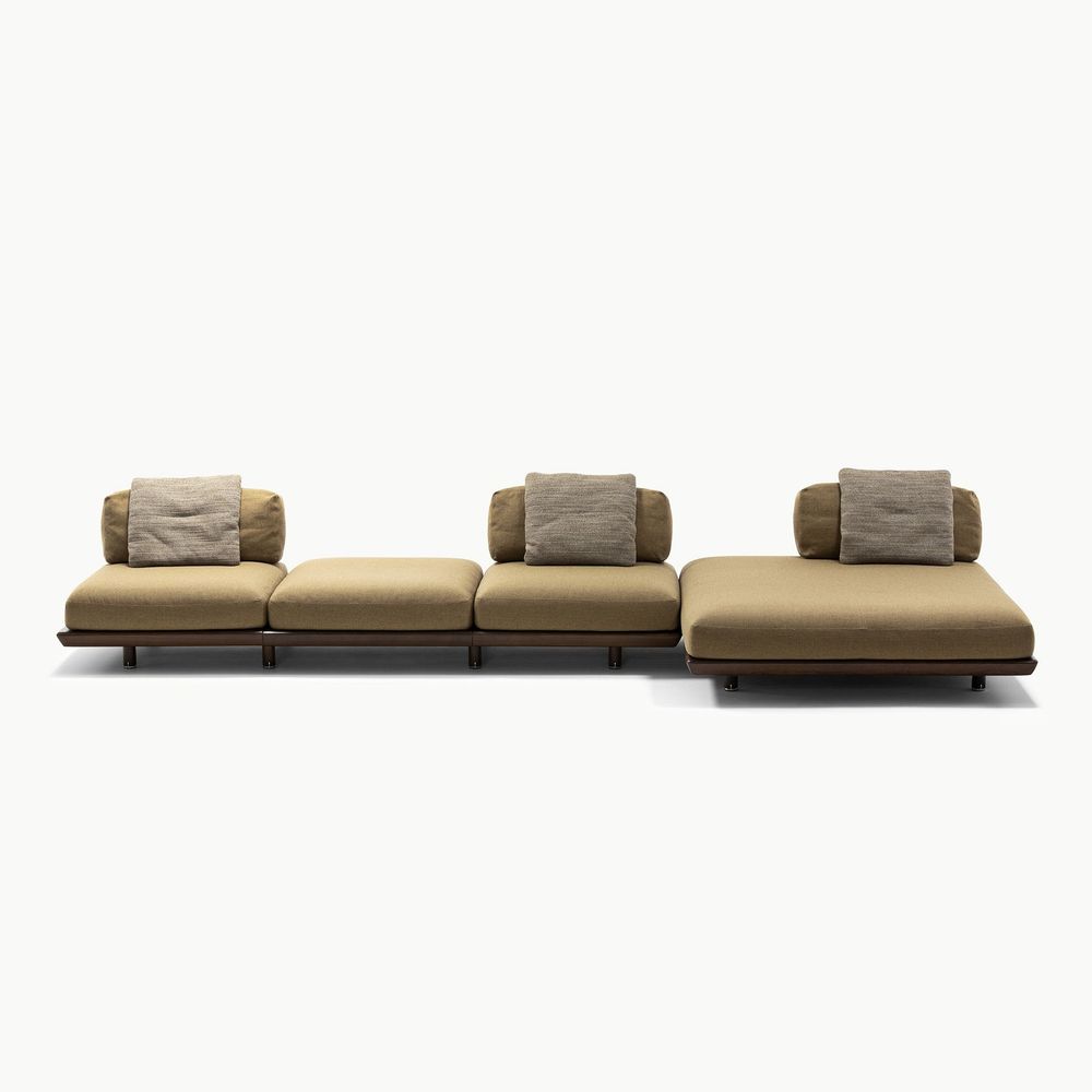 Modular Caprera sofa composition featuring soft beige upholstery with warm brown back cushions and a dark wood base creating a low elegant profile and flexible seating layout with a calm neutral palette.
