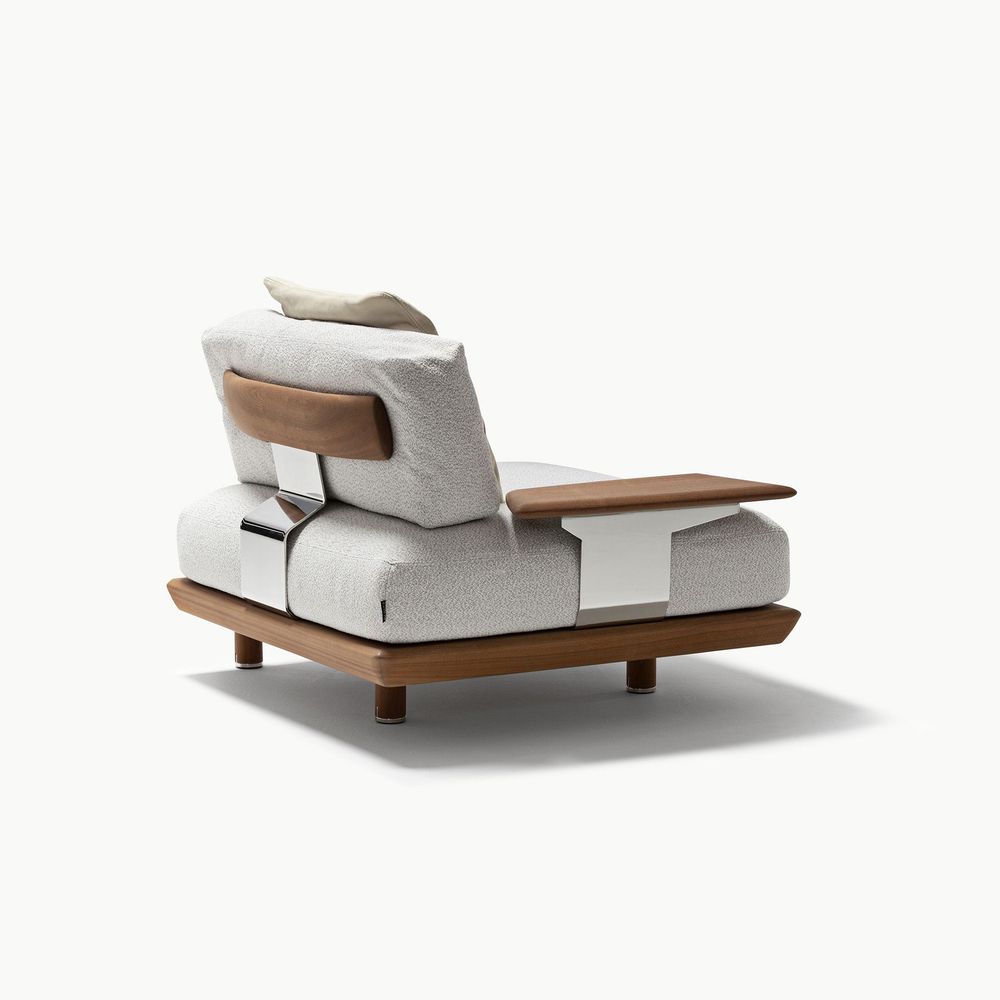 Caprera sofa module shown from the side with light ivory fabric upholstery warm walnut wood base and armrest and soft neutral cushions highlighting its sculptural form and refined material contrast.