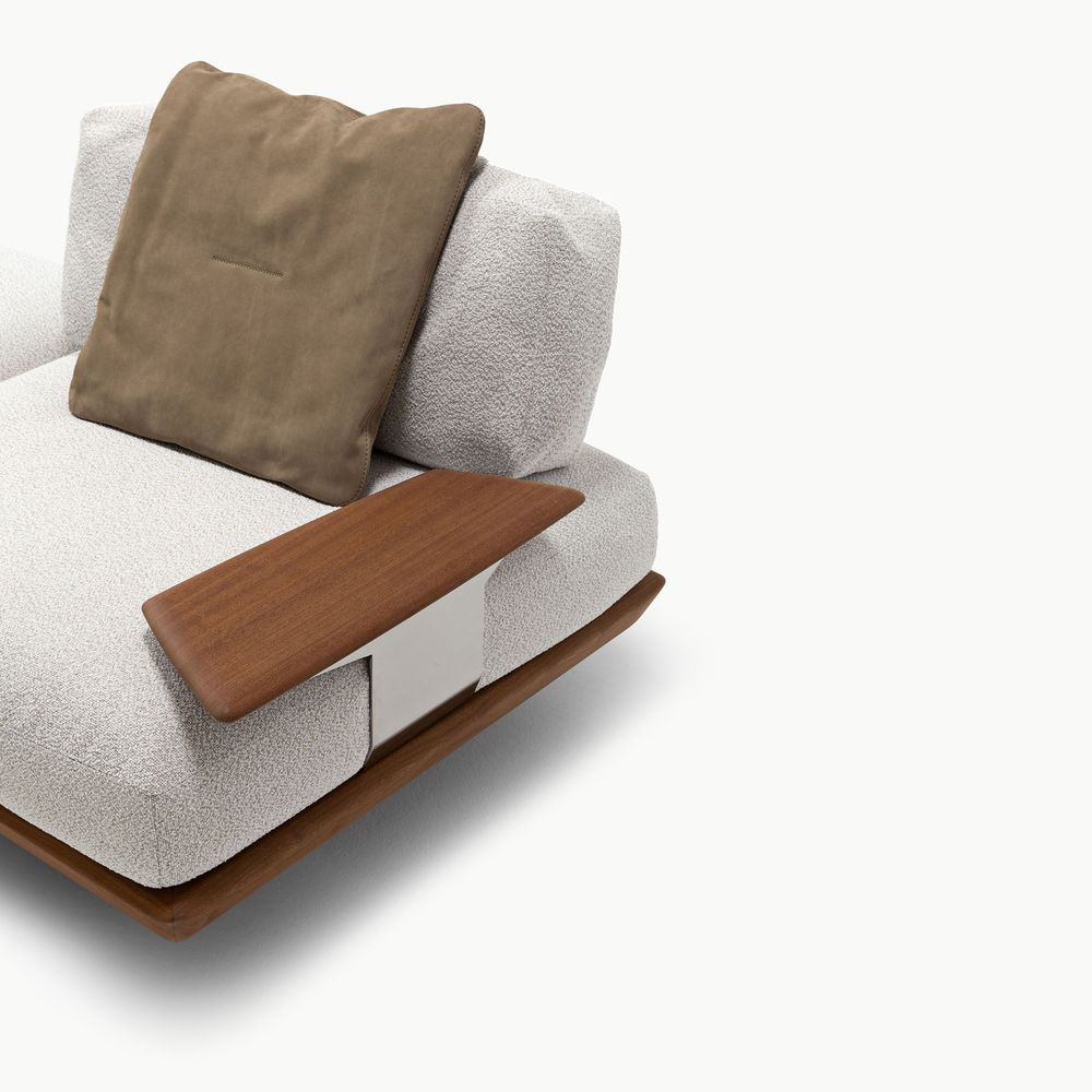 Caprera sofa detail featuring light ivory fabric upholstery paired with a soft brown cushion and a smooth walnut wood armrest creating a refined contrast of warm and neutral tones with a clean modern finish.