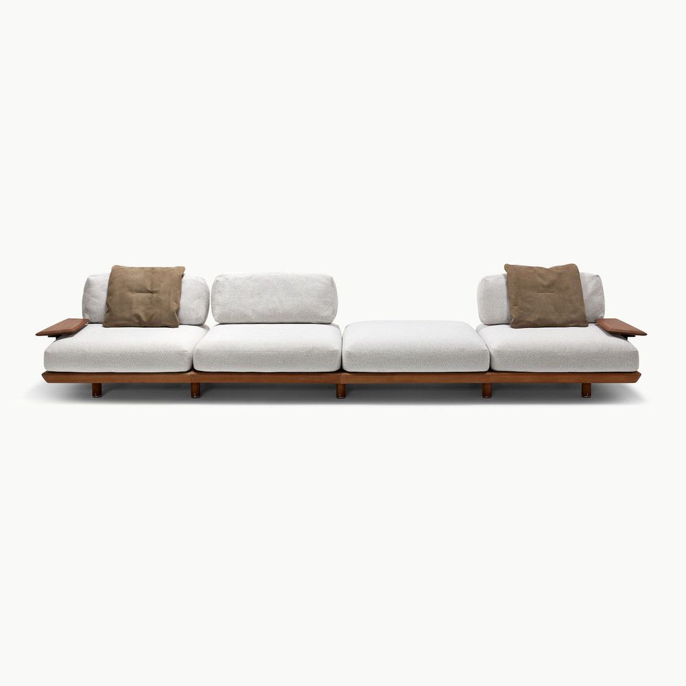 Large Caprera sofa with a low profile silhouette featuring plush upholstered cushions a warm wood base and integrated side surfaces offering a relaxed contemporary look designed for spacious modern living areas.