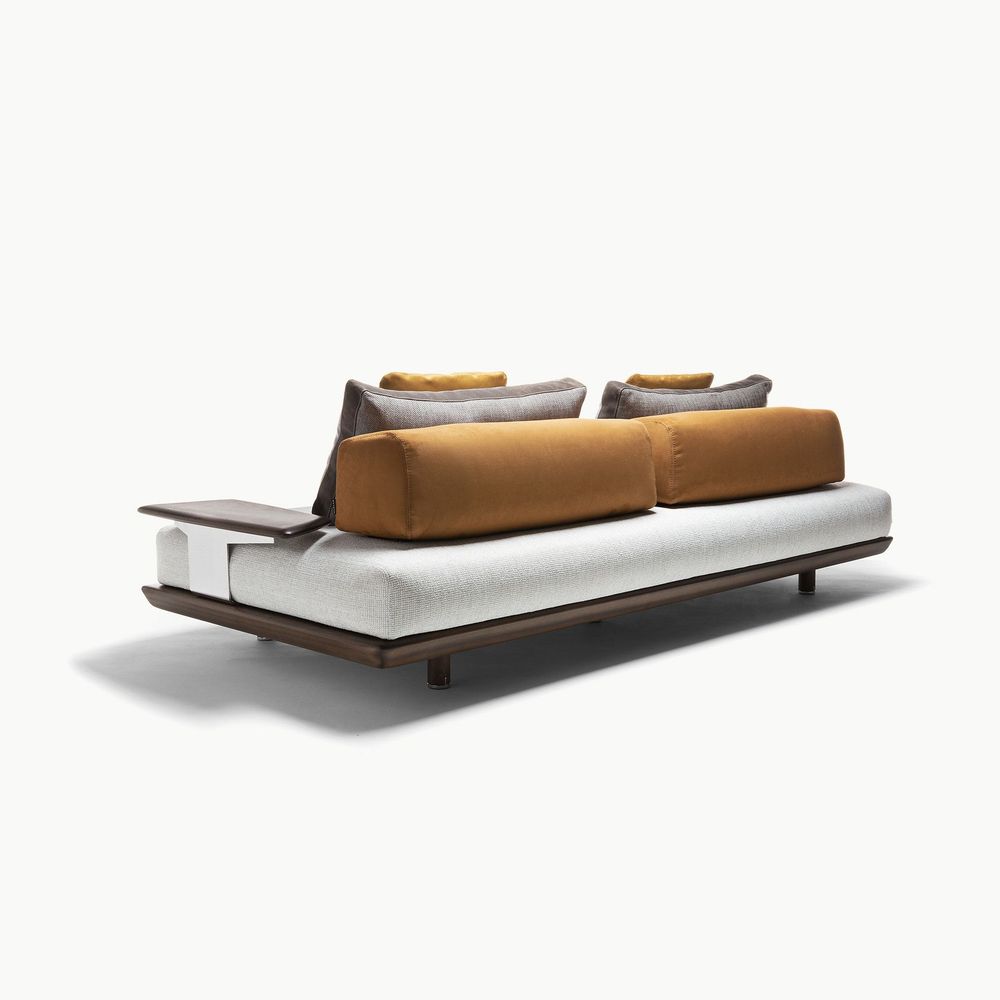 Caprera sofa shown from the rear featuring light upholstery paired with warm tan and brown back cushions plus a dark wood side surface creating a clean sculptural look with subtle contrast for modern interiors.