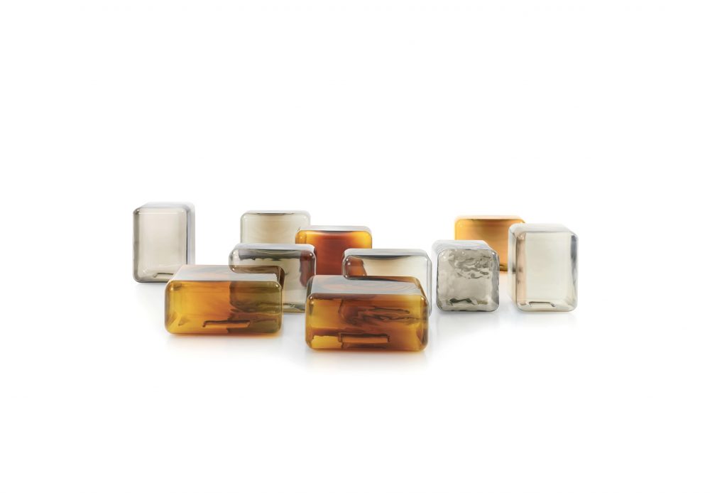 A collection of sculptural glass tables in warm amber and soft neutral tones creates a dynamic, light-filled arrangement. Their rounded forms and translucent finishes bring depth, reflection, and a subtle sense of movement to the space.