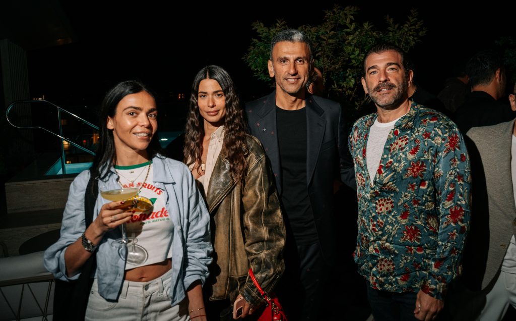 A stylish group gathers at an evening event, posing with relaxed confidence. Warm lighting, bold textures, and a mix of tailored and casual looks create a vibrant, social atmosphere with a contemporary, cosmopolitan edge.